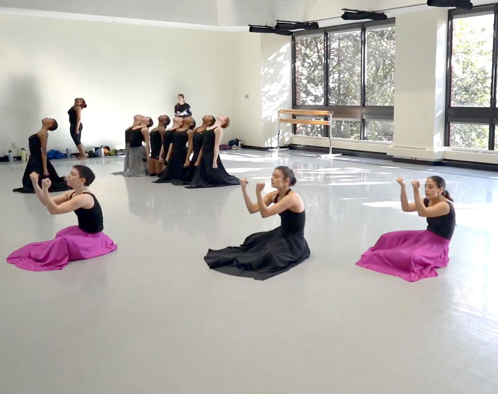 Mason dancers dressed in black and pink, 3 sitting on ground with arms upwards and fists clenched, the other dancers behind kneeling