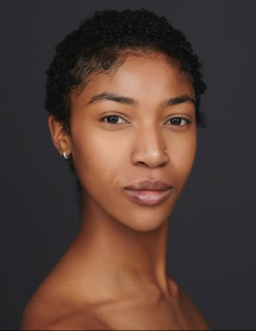 An African-American woman with short hair and bare shoulders looks at the camera