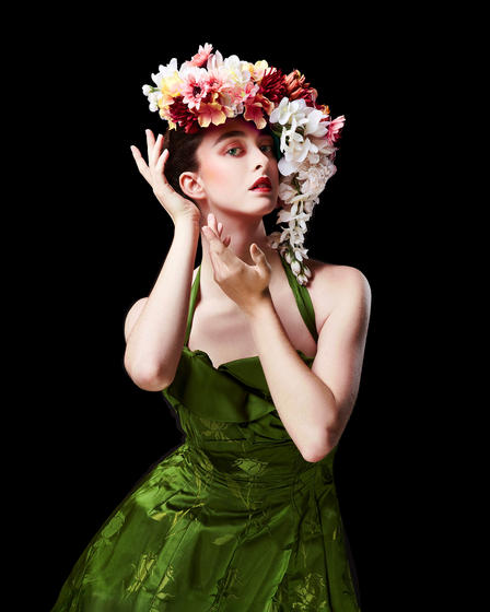 Mason School of Dance student in green dress with flower arrangement on head posing against black background