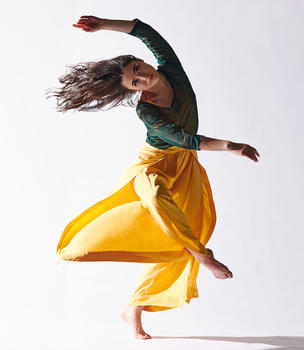 Mason dancer with long brown hair dressed in yellow and green against a white background